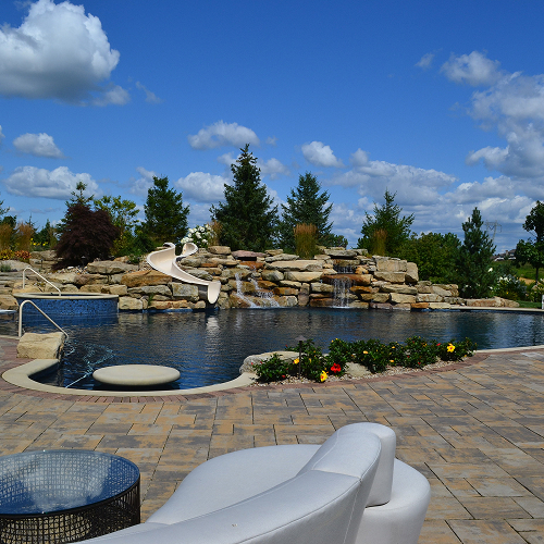 Luxury backyard resort with custom swimming pool, natural stone waterfall, waterslide, and paver patio landscape design.